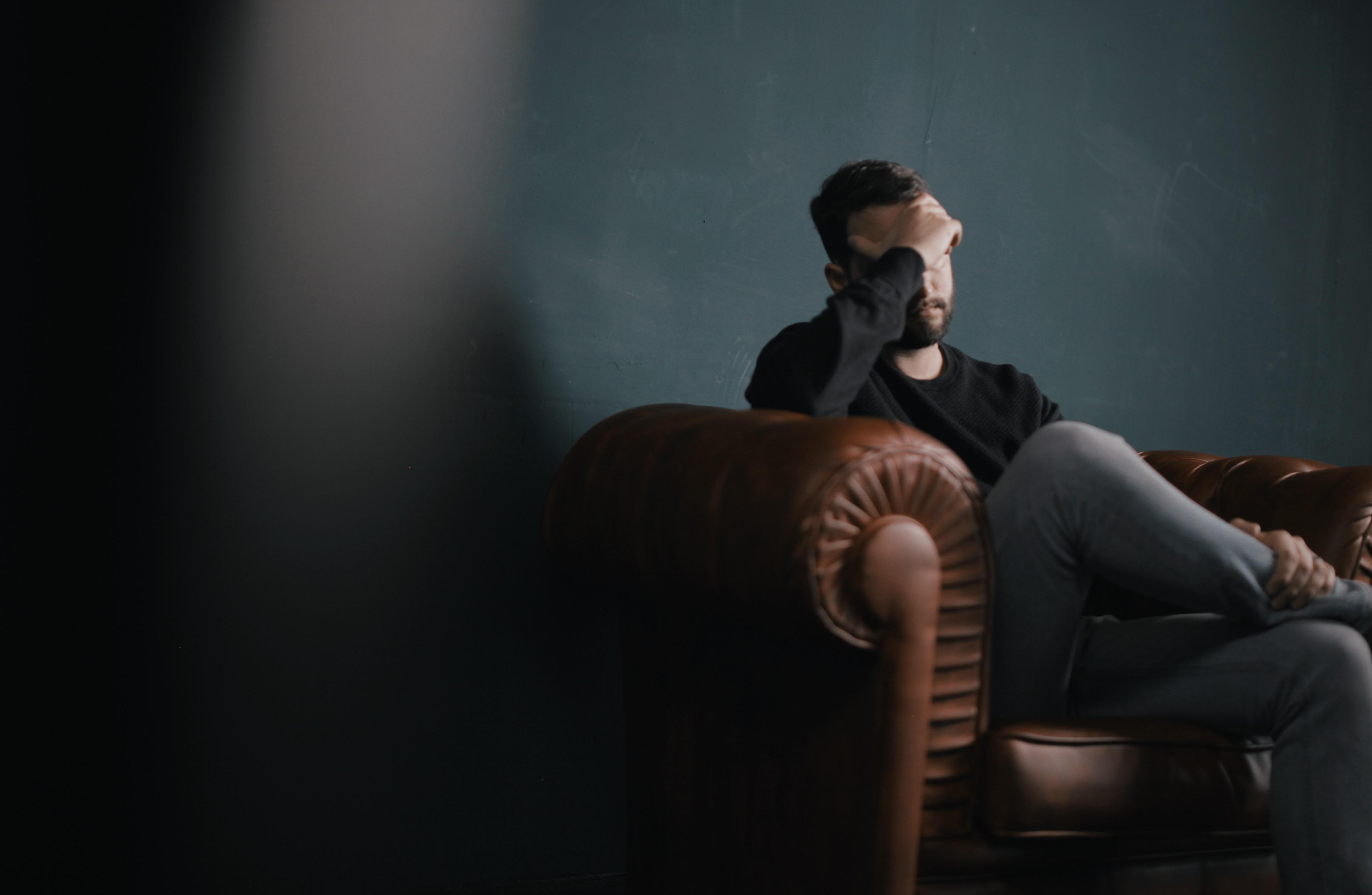 Man on sofa holds head in hand